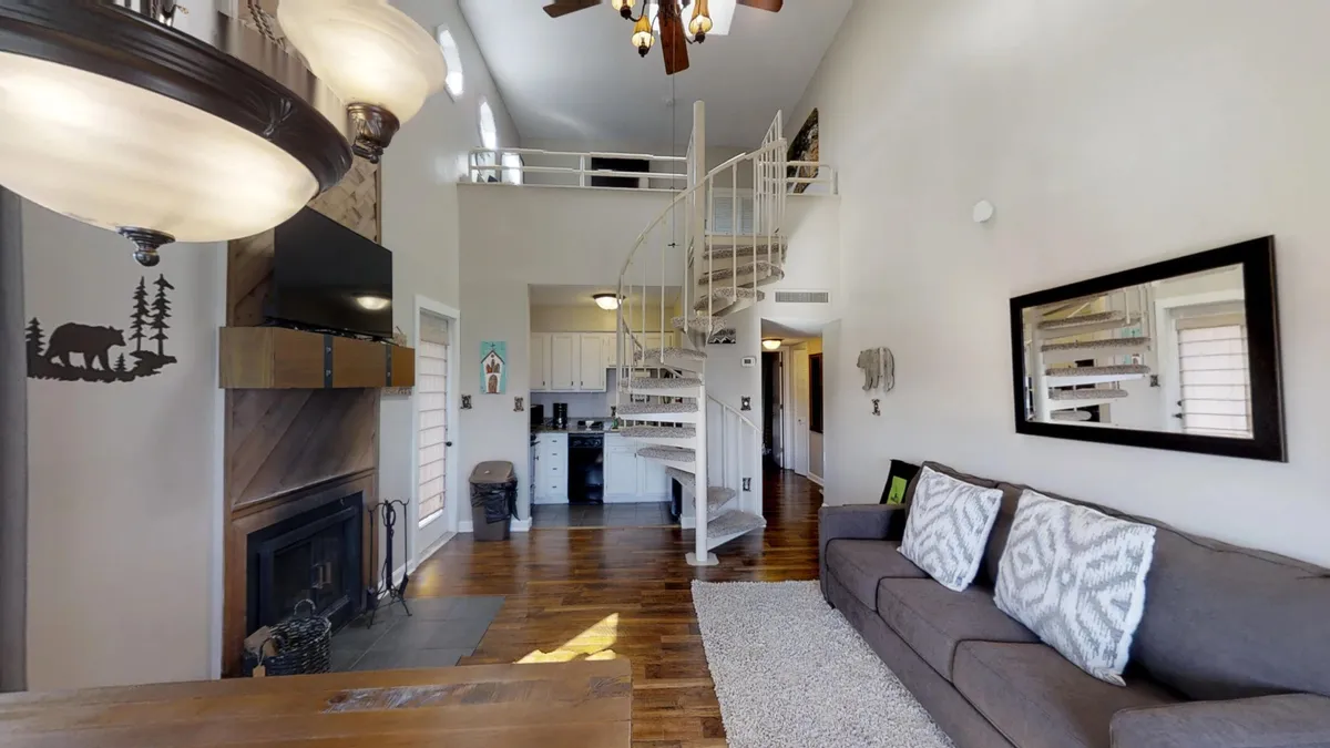 An open-plan living and dining area featuring a spiral staircase, a cozy fireplace, a comfortable sofa, and a dining table. The space evokes warmth and intimacy, ideal for shared meals, conversation, and evening relaxation.