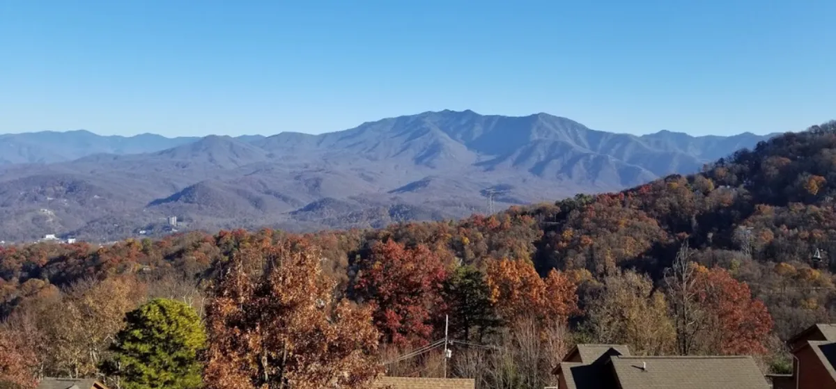 A sweeping view of a mountain range with rich autumn foliage under a clear blue sky. The scene embodies tranquil beauty and the changing colors of fall, inviting guests to explore and enjoy nature's splendor.