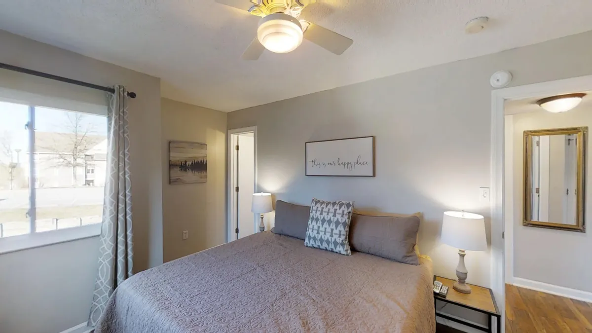 A serene bedroom featuring a neatly made bed adorned with decorative pillows, warm bedside lamps, tasteful wall art with an inspirational quote, and a window letting in natural light. The overall atmosphere is calming and inviting—perfect for unwinding after a day of adventure.