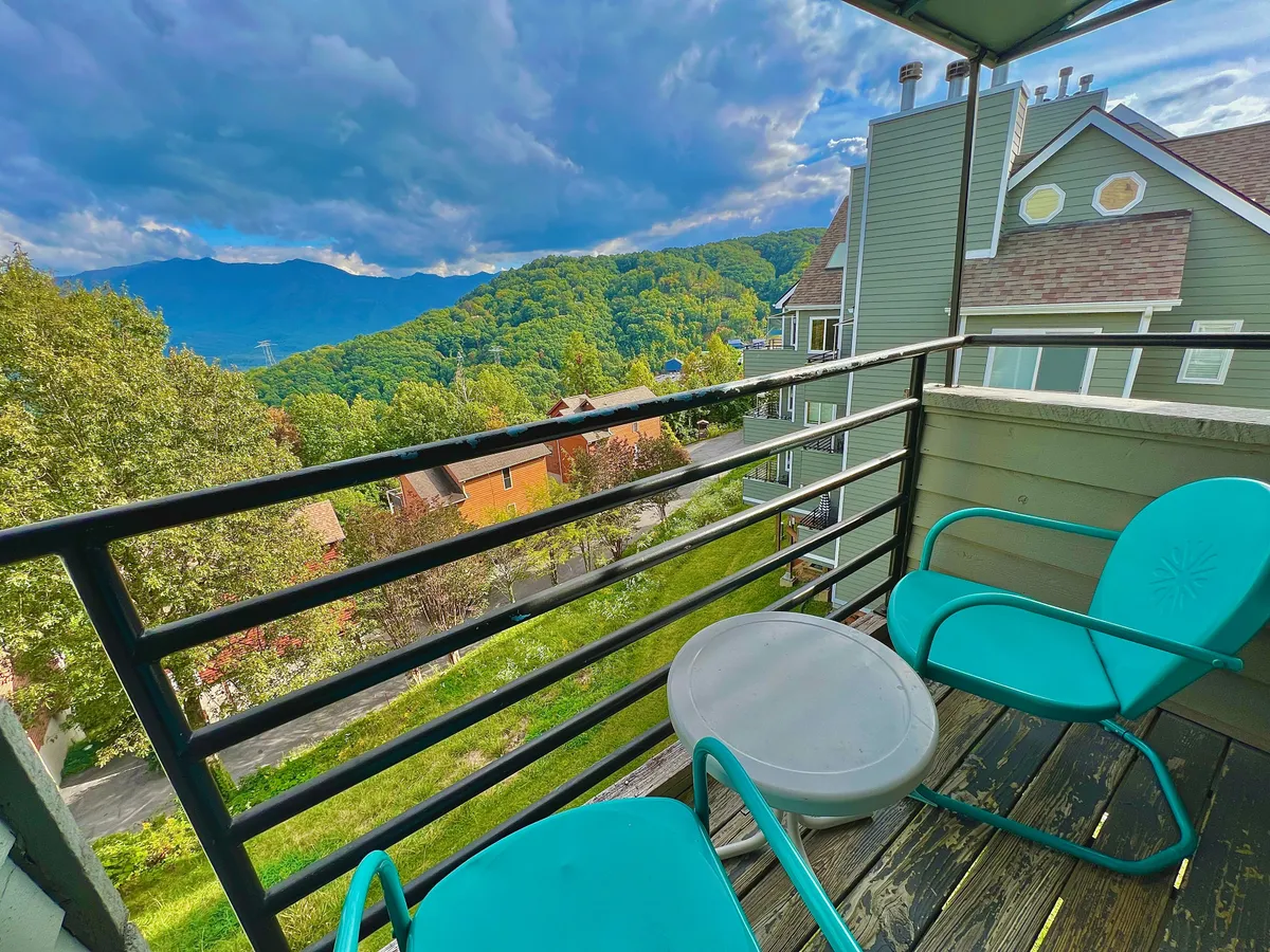 An inviting exterior shot highlighting a balcony with a sturdy railing, comfortable seating area, and expansive panoramic mountain views. The setting evokes relaxation and family togetherness, with hints of enjoying both sunrise and sunset in a communal outdoor space.