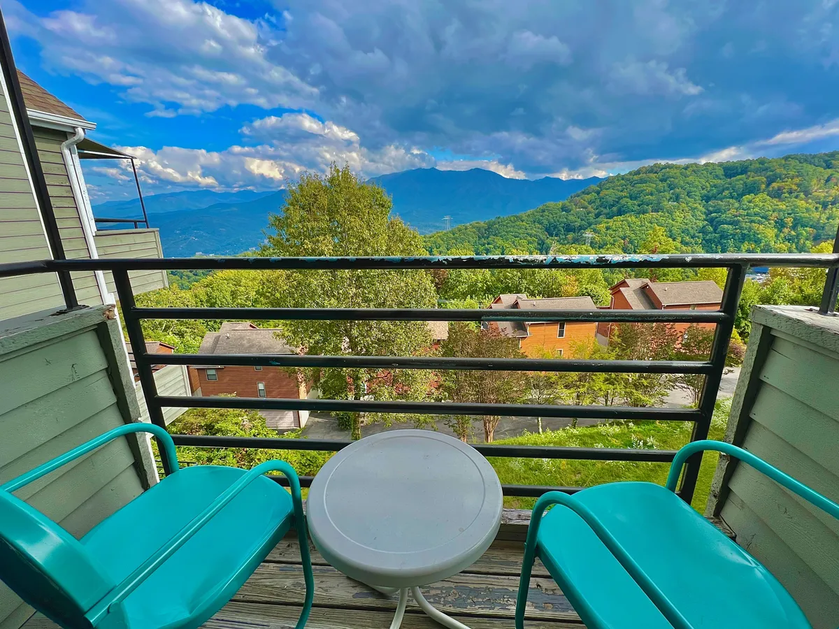 This image features a balcony with seating overlooking a wide, serene mountain view beneath a cloudy sky. The outdoor setting suggests a peaceful spot perfect for enjoying morning coffee or unwinding with a glass of wine while taking in the stunning Smoky Mountains panorama.