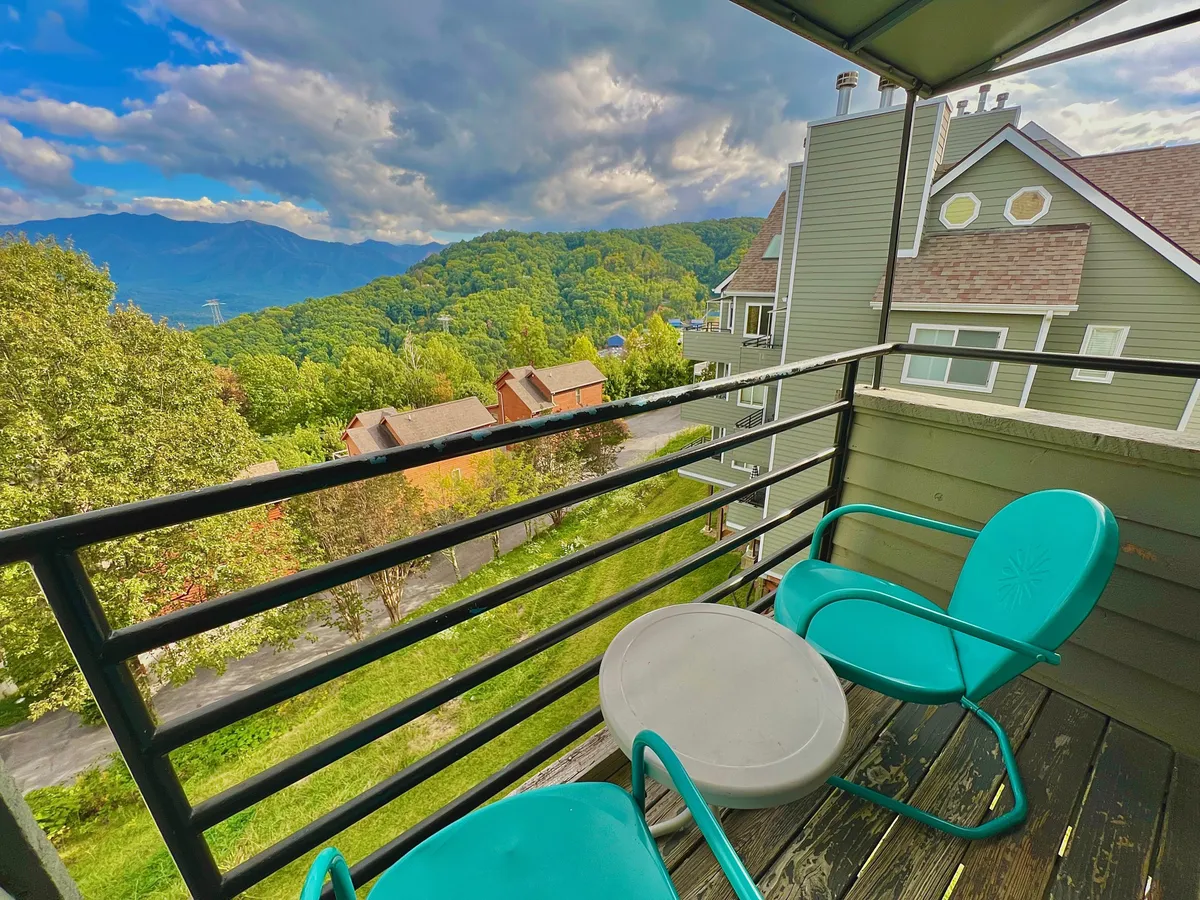 This image features a serene exterior view from a balcony furnished with comfortable seating, overlooking the rolling Smoky Mountains under a cloudy sky. The space is inviting for relaxation, with opportunities for morning coffee, evening chats, and stargazing that echo the tranquil natural beauty surrounding the property.