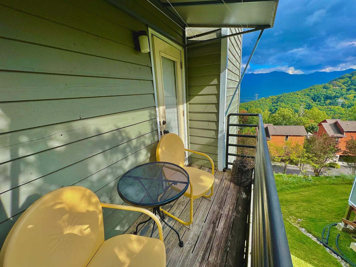 An exterior shot of a balcony furnished with yellow chairs and a black table, set against a backdrop of mountains. The arrangement suggests a cozy, private spot to enjoy the outdoors and share quiet moments while admiring the sunset.